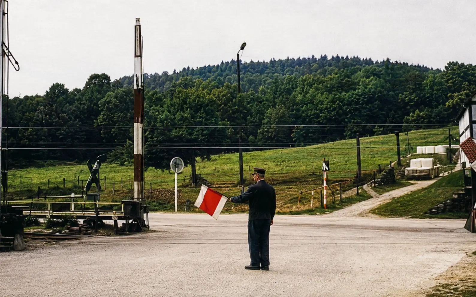Photo of level crossing with barriers down and railway worker holding red flag