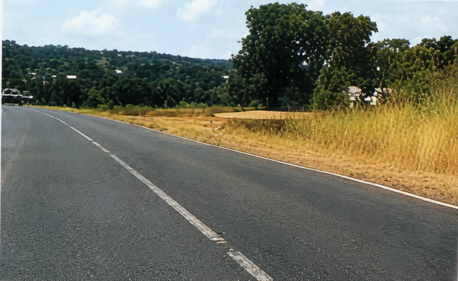 two lane road with a car infront, on a dry clear day with dust on the road