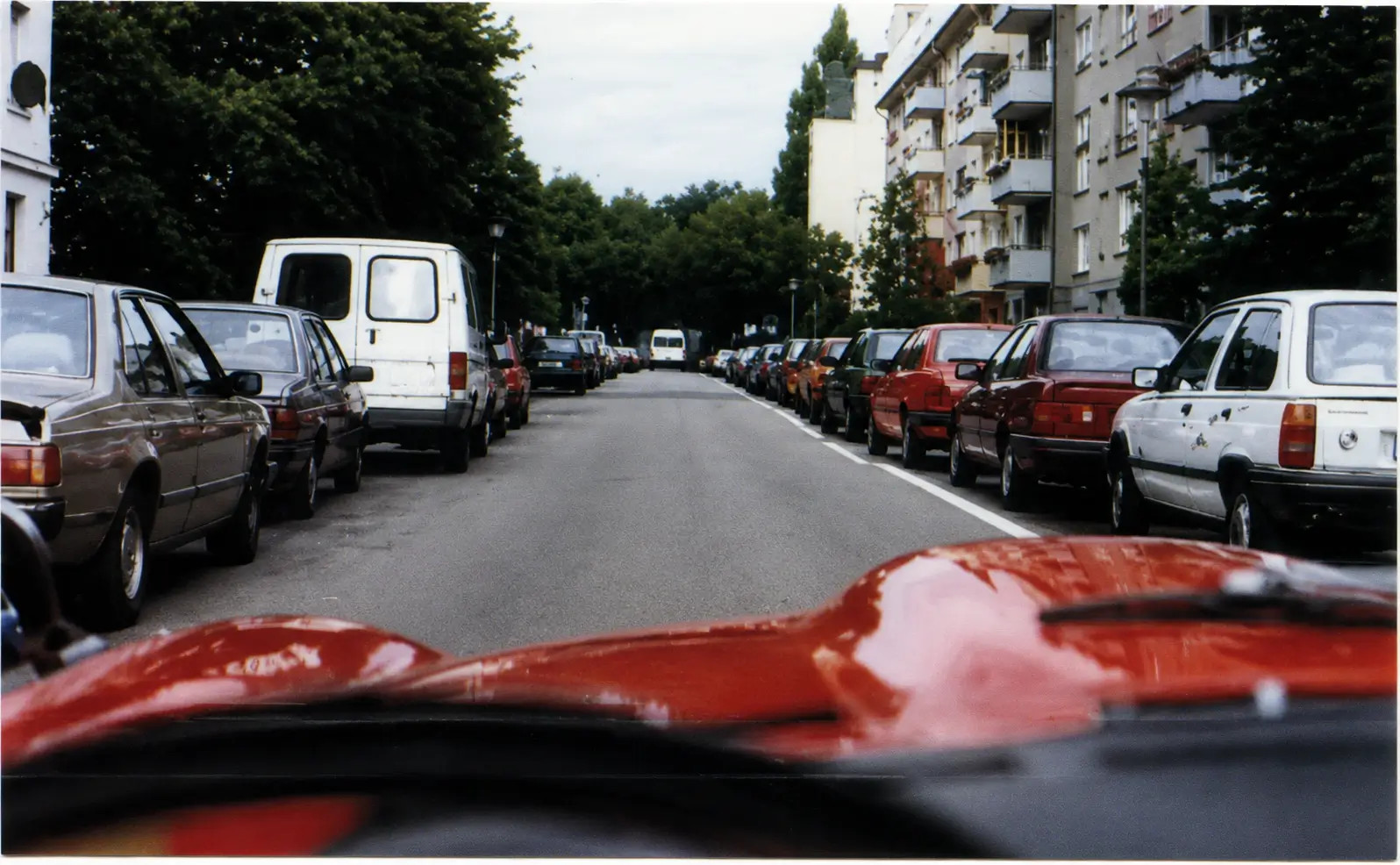 driving past parked cars on both sides of the road in a built up area