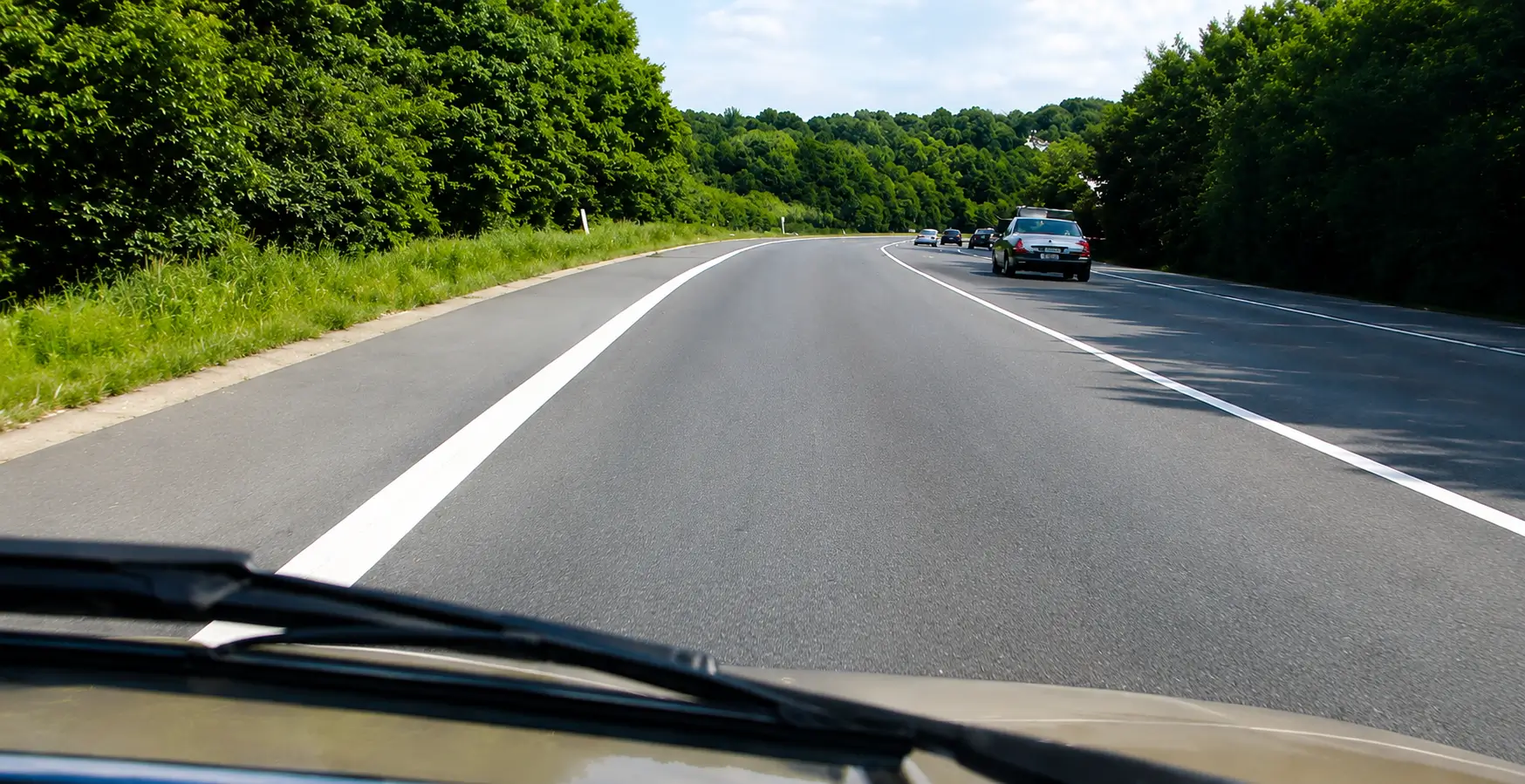 Vehicles driving along a dual carriageway bordered by trees and grass