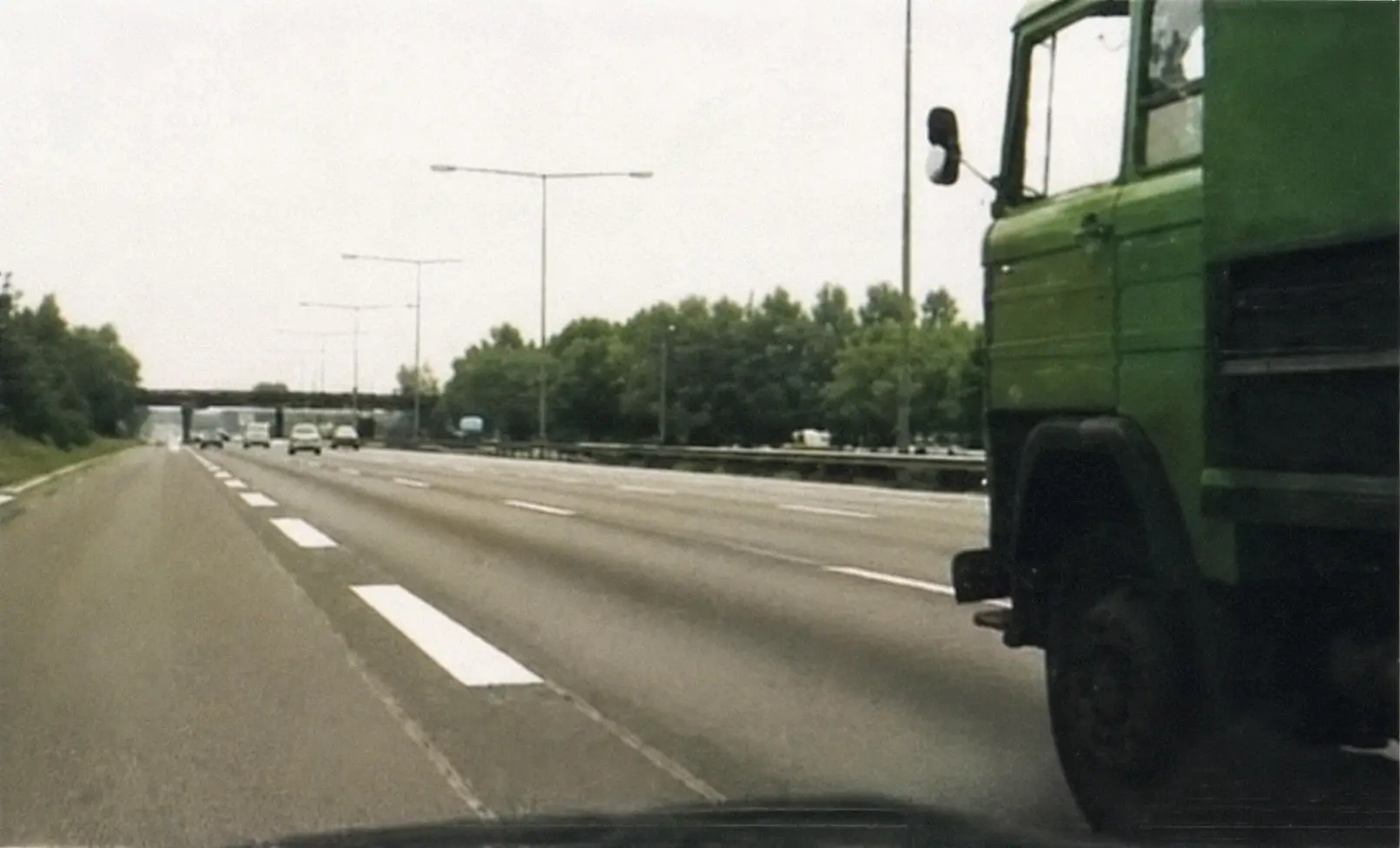Highway view from inside a vehicle with green truck on the right and overpass ahead