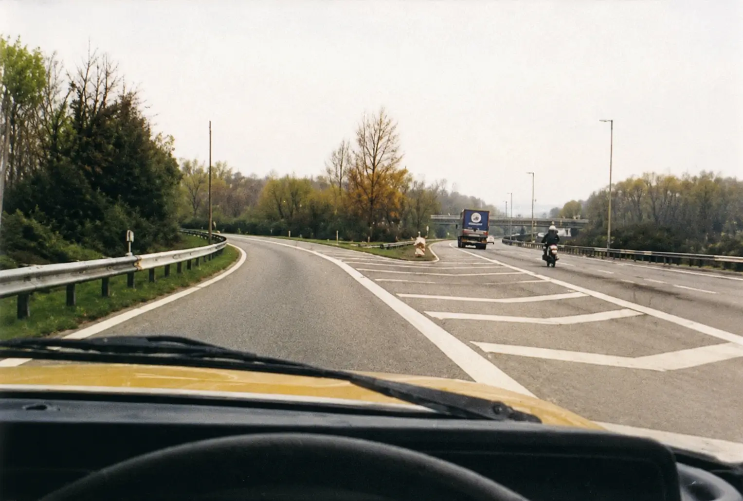 Driver's view of curved highway with truck and motorcycle ahead and chevron road markings
